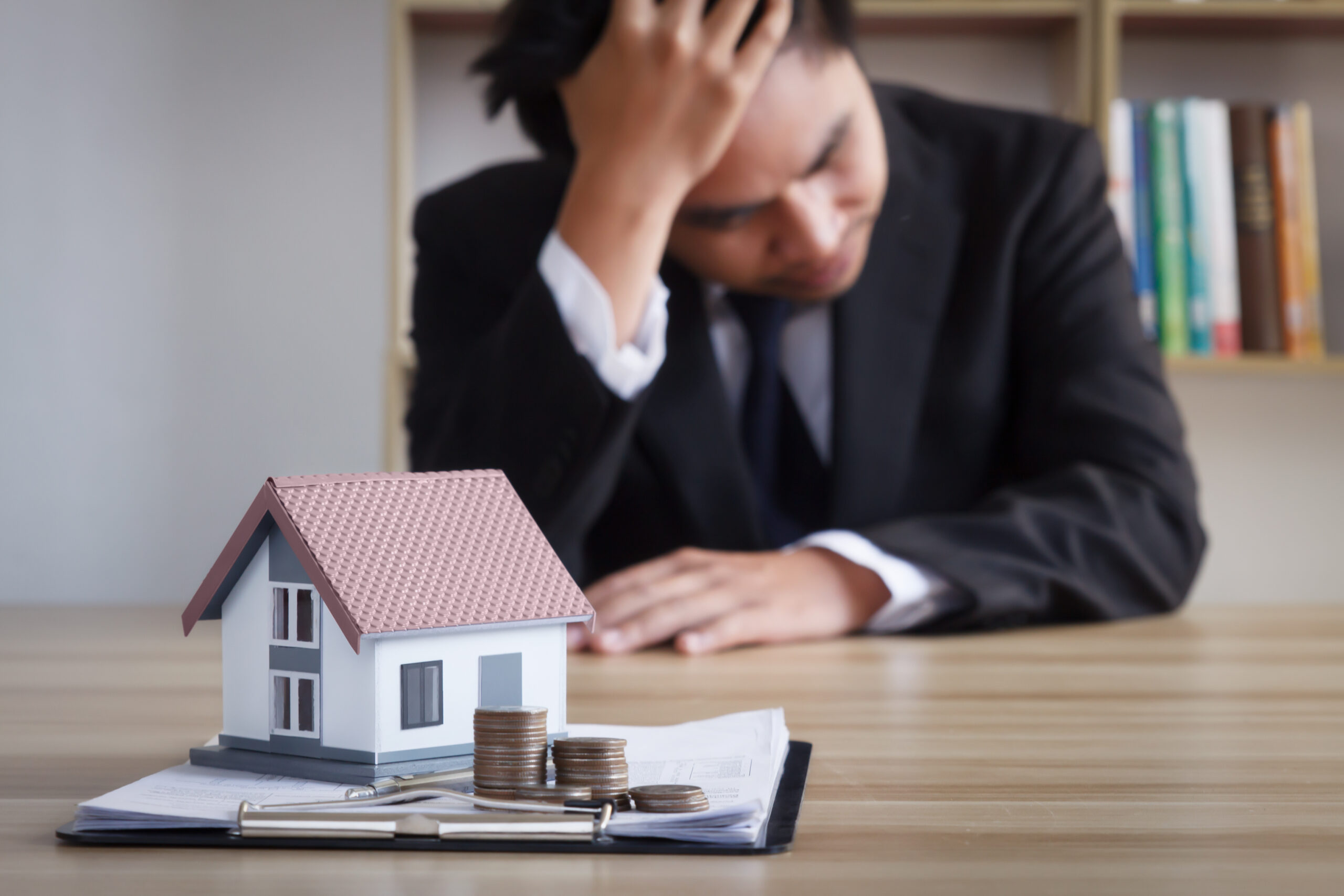 Young businessman sits depressed with a model of a house in front of him, the concept of real estate debt spreading around the world.  rising interest rates  world economic crisis